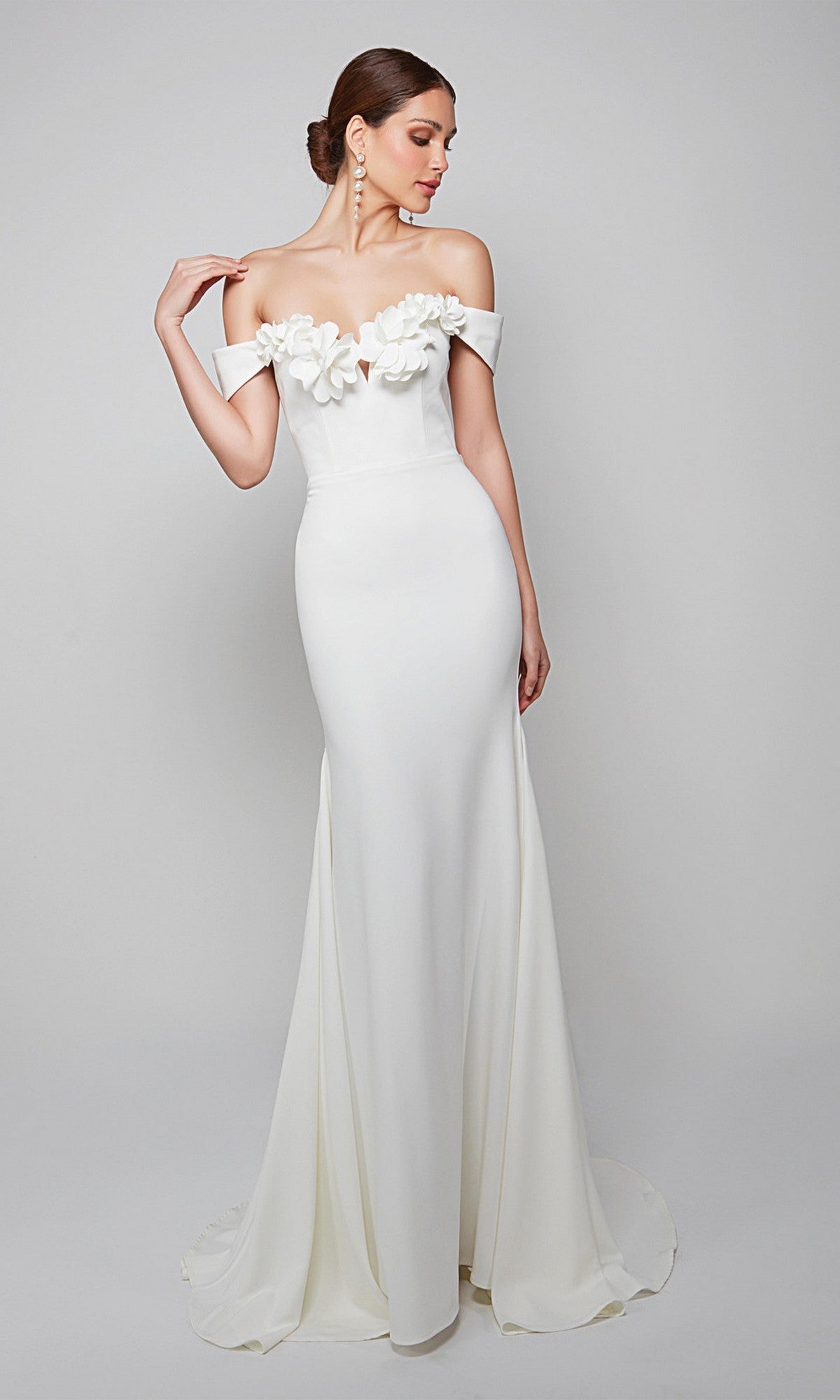 A woman in the Alyce 7062 long formal dress, diamond white, with an off-the-shoulder neckline and elegant 3D floral accents along the top, stands against a plain background.
